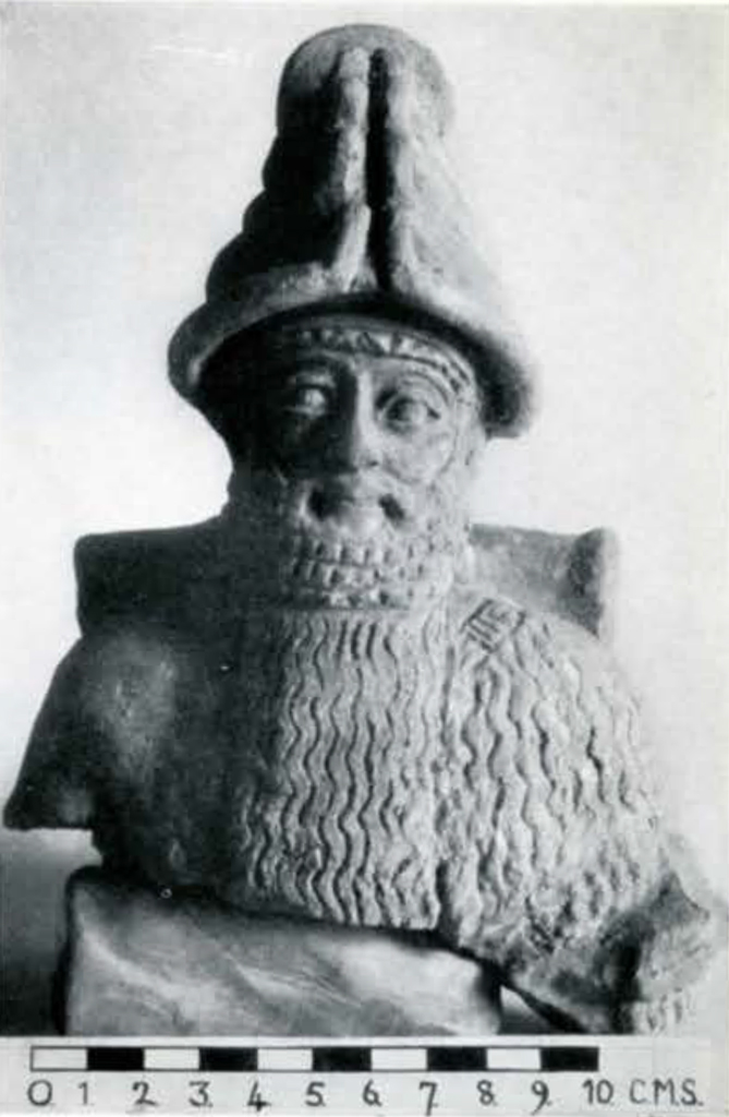 The torso and head of a statuette of a god with a very long beard and a conical hat with a split down the middle front