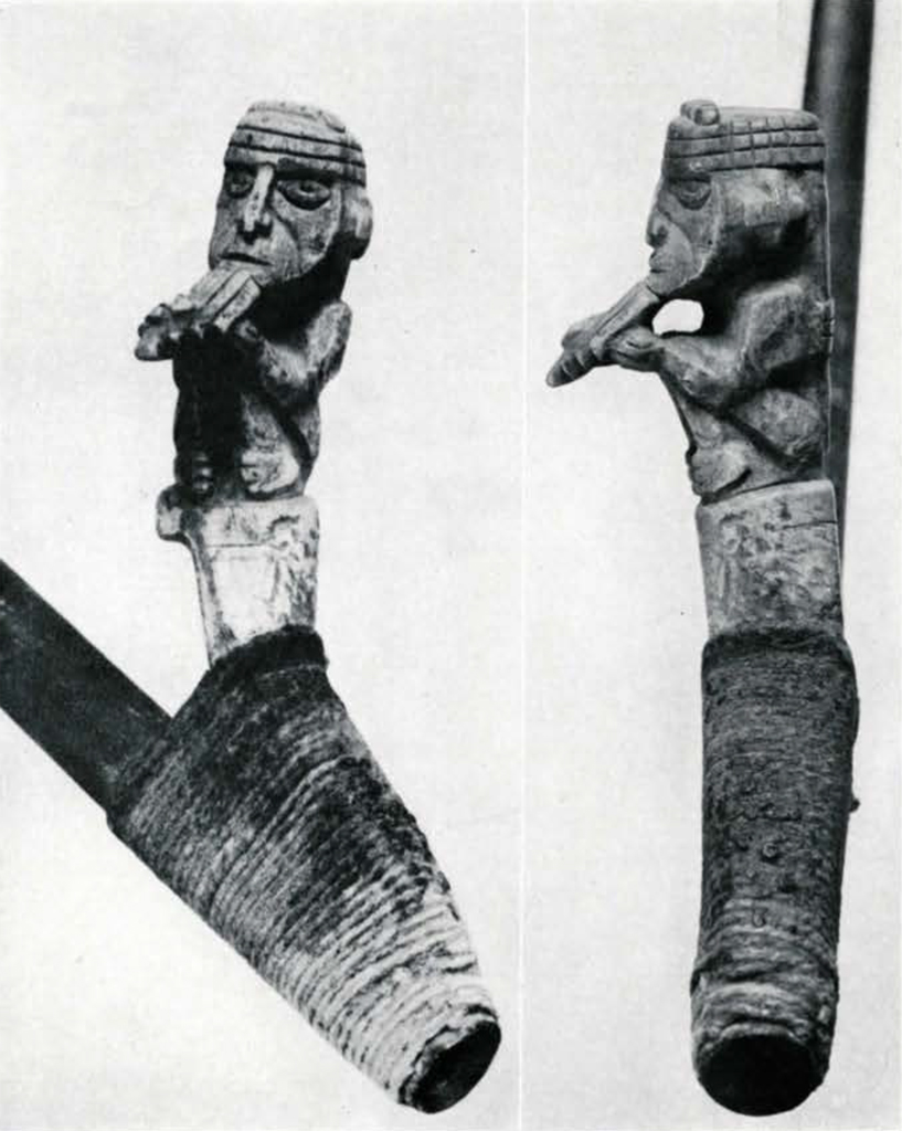 Close up of a figure carved into a spearthrower handle grip, the figure is playing the pan pipes