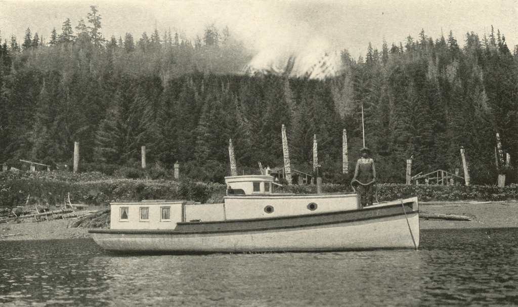 A boat in a harbor, a man standing on the boat, dense pine forest and totem poles in the background