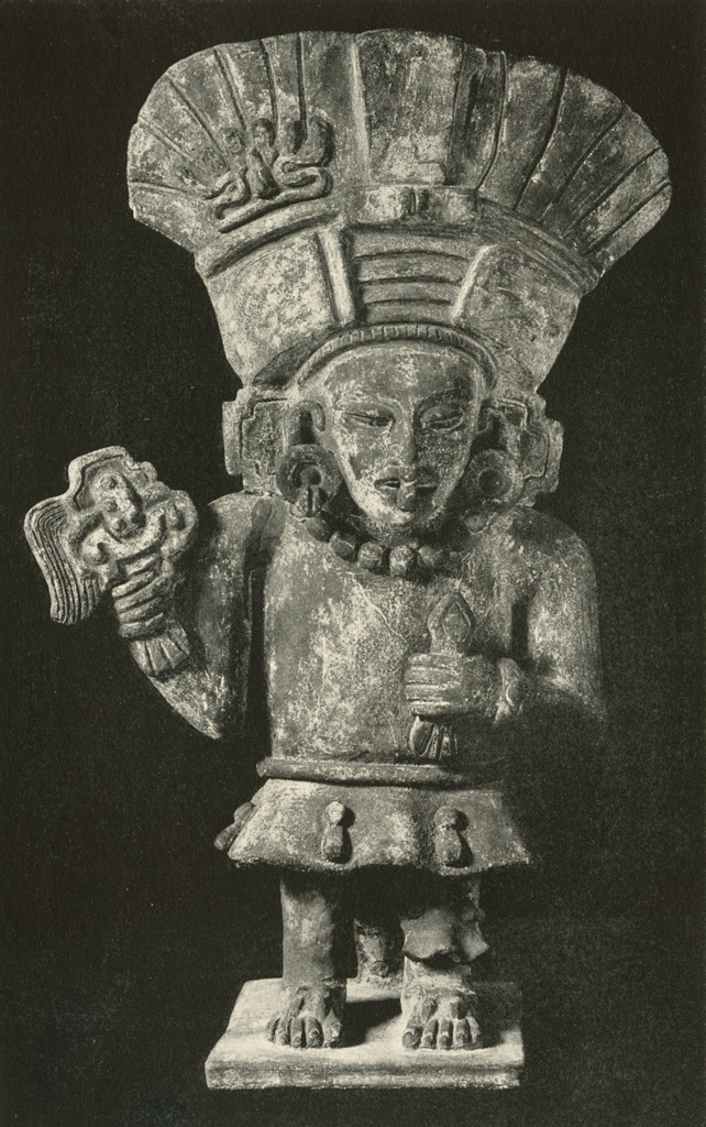Effigy urn in the shape of a standing man with a large flared headdress and holding an object in one hand