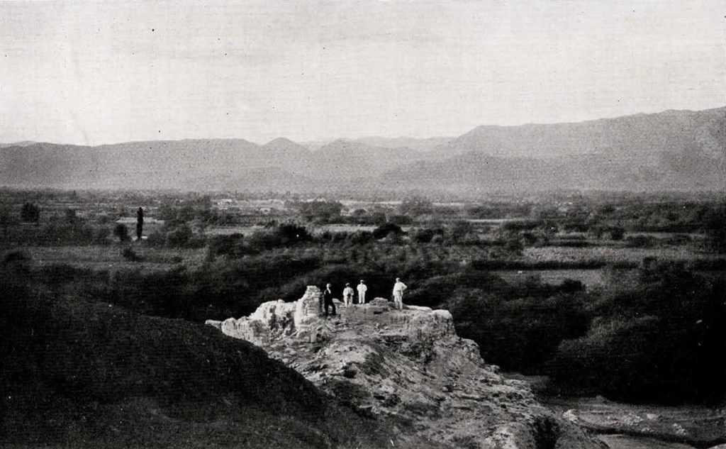 View of a valley with people standing upon a citadel ruin in the foreground