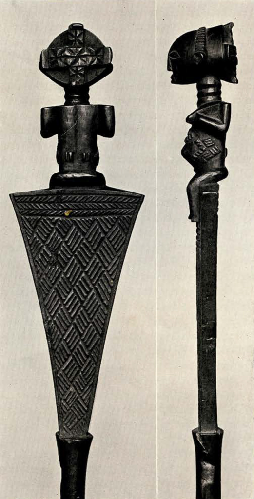Close up of seated female figure at the top of triangular shape of staff